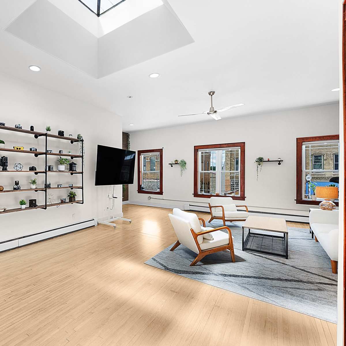 A spacious living room features a vaulted ceiling, large windows, and a shelving unit displaying decor items.