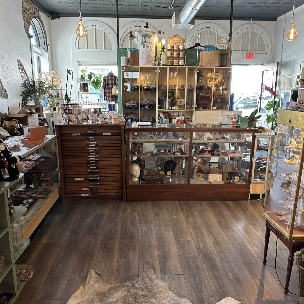 The interior of a boutique, featuring glass display cases filled with various items, wooden furniture, and a bright atmosphere.