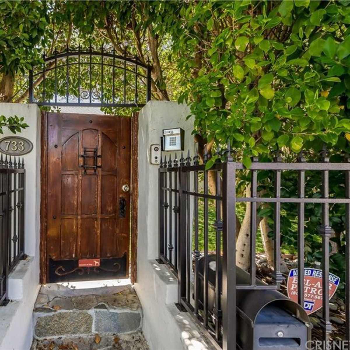 A wooden door with a wrought iron gate is framed by lush greenery, leading to a pathway.