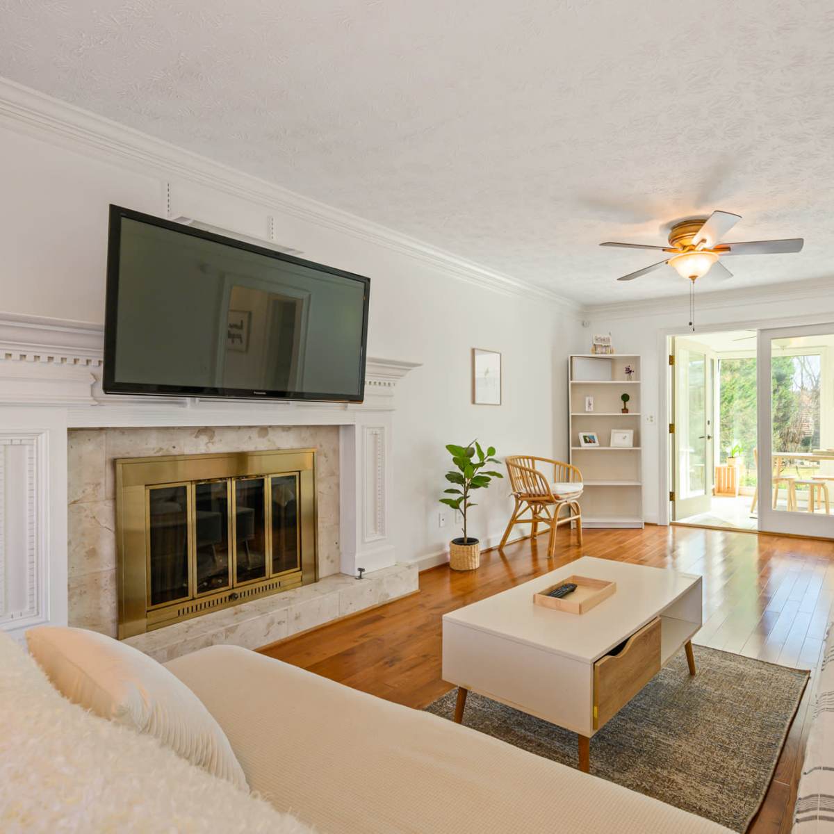 A modern living room features a large television mounted above a fireplace, a coffee table, two couches, and doors leading to a patio.