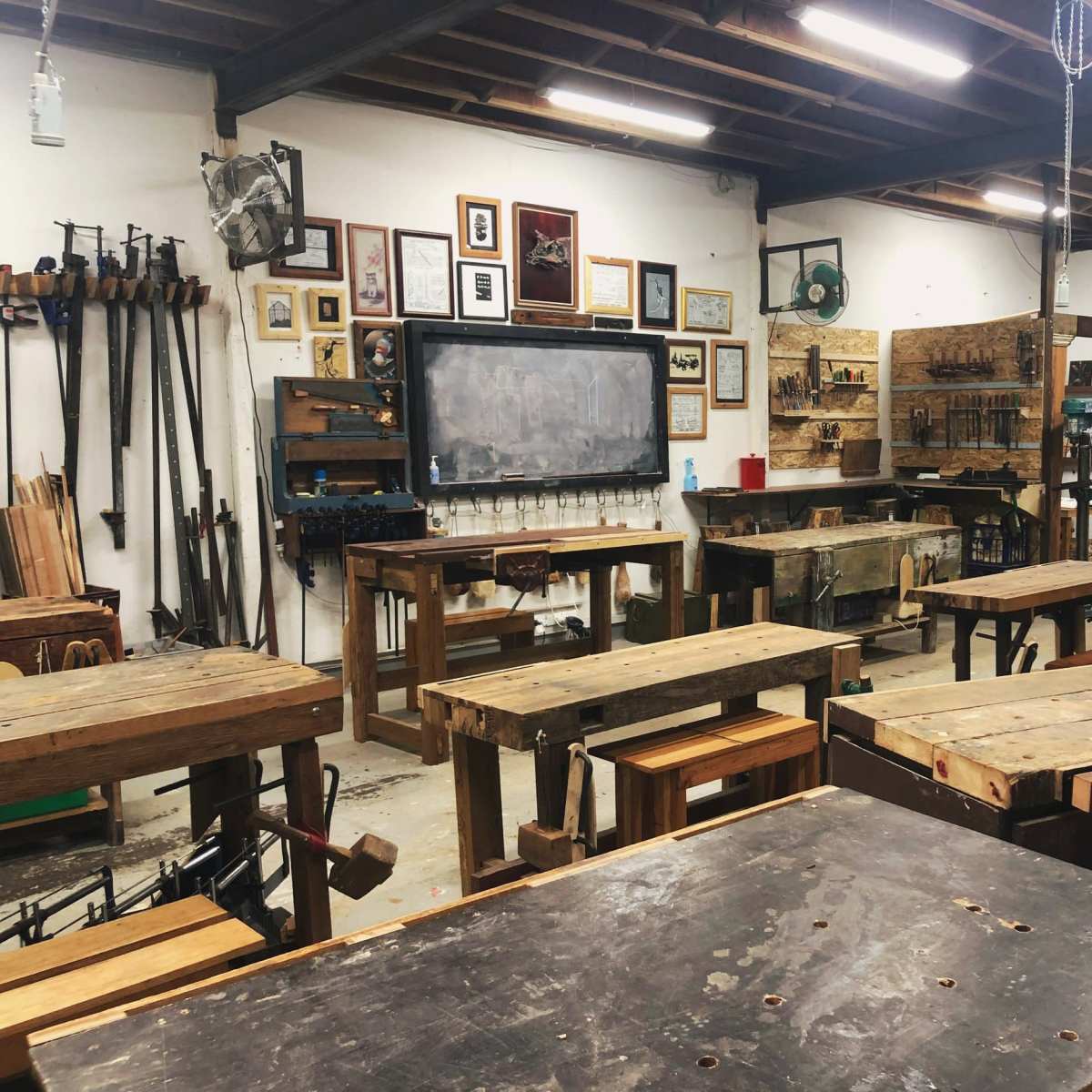 A woodworking shop filled with various wooden workbenches, tools, and framed pictures on the walls.