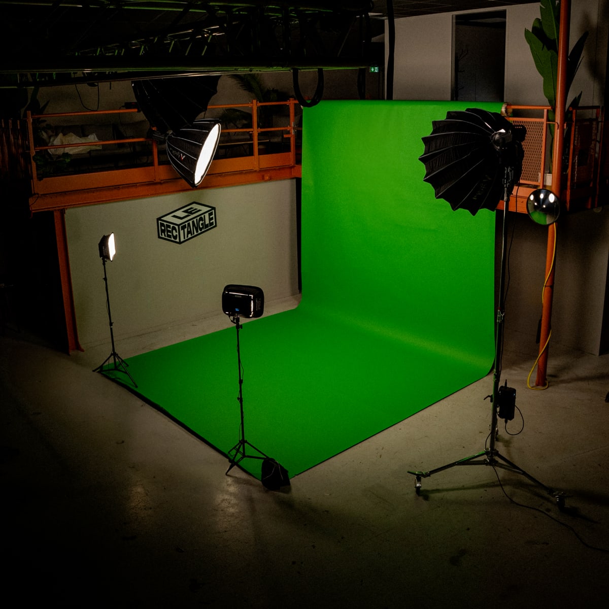 A photography studio with a green backdrop and various lighting equipment set up.