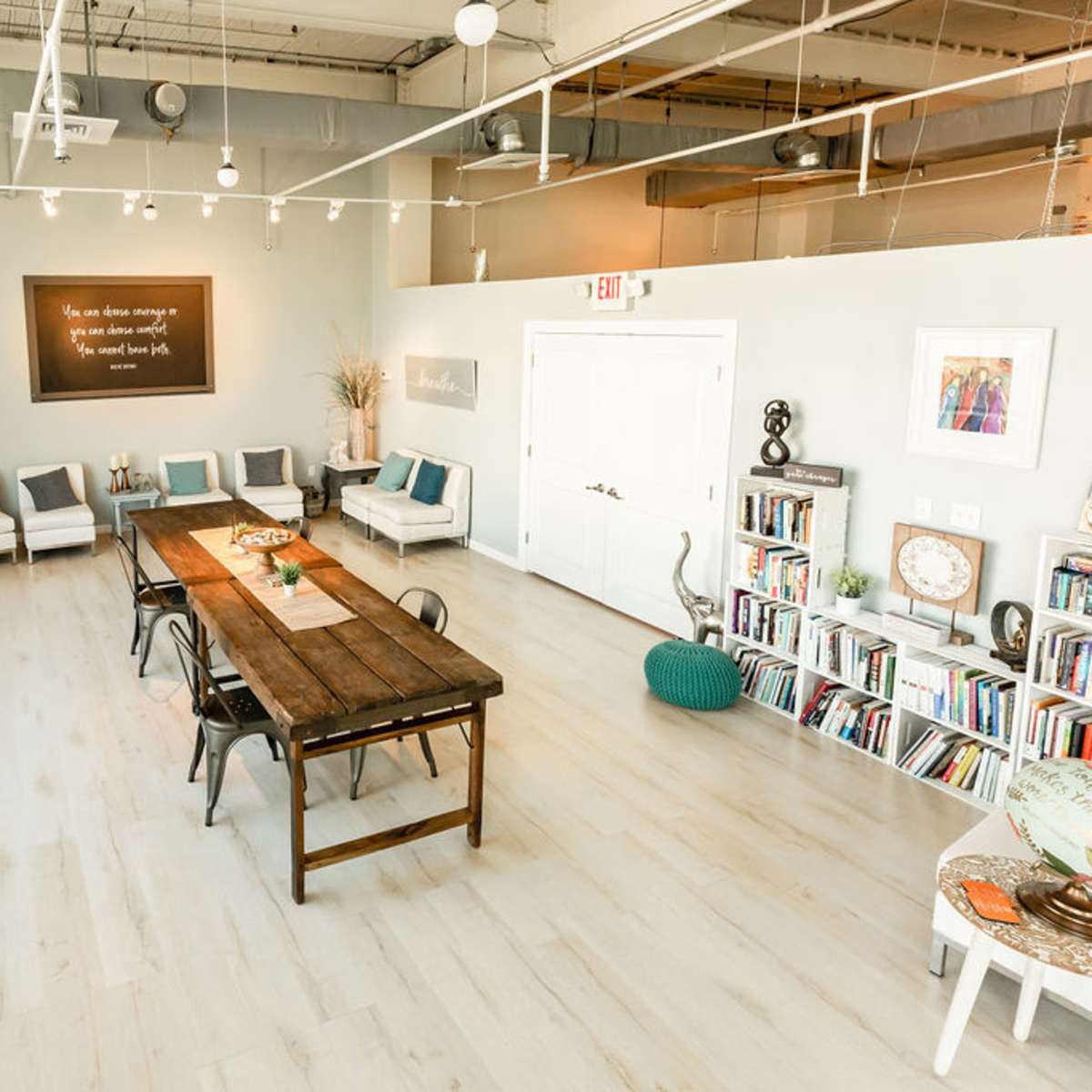 A well-lit, spacious room with a long wooden table at its center surrounded by chairs, and white sofas arranged along the walls.