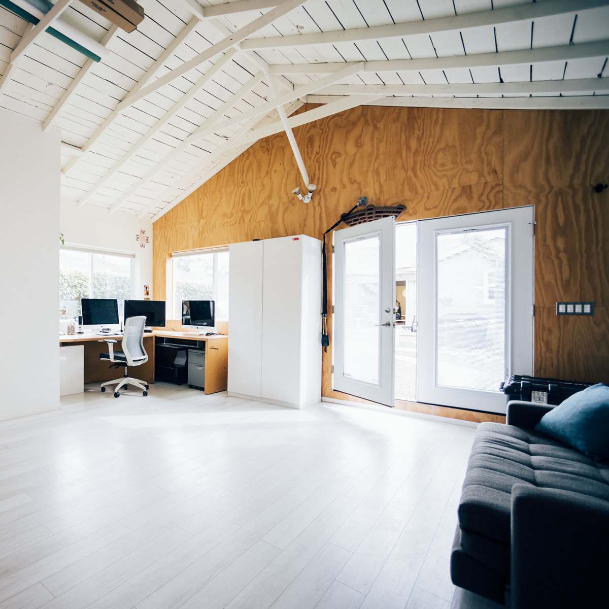 A spacious, light-filled interior featuring a home office area with two desks and a comfortable seating area.