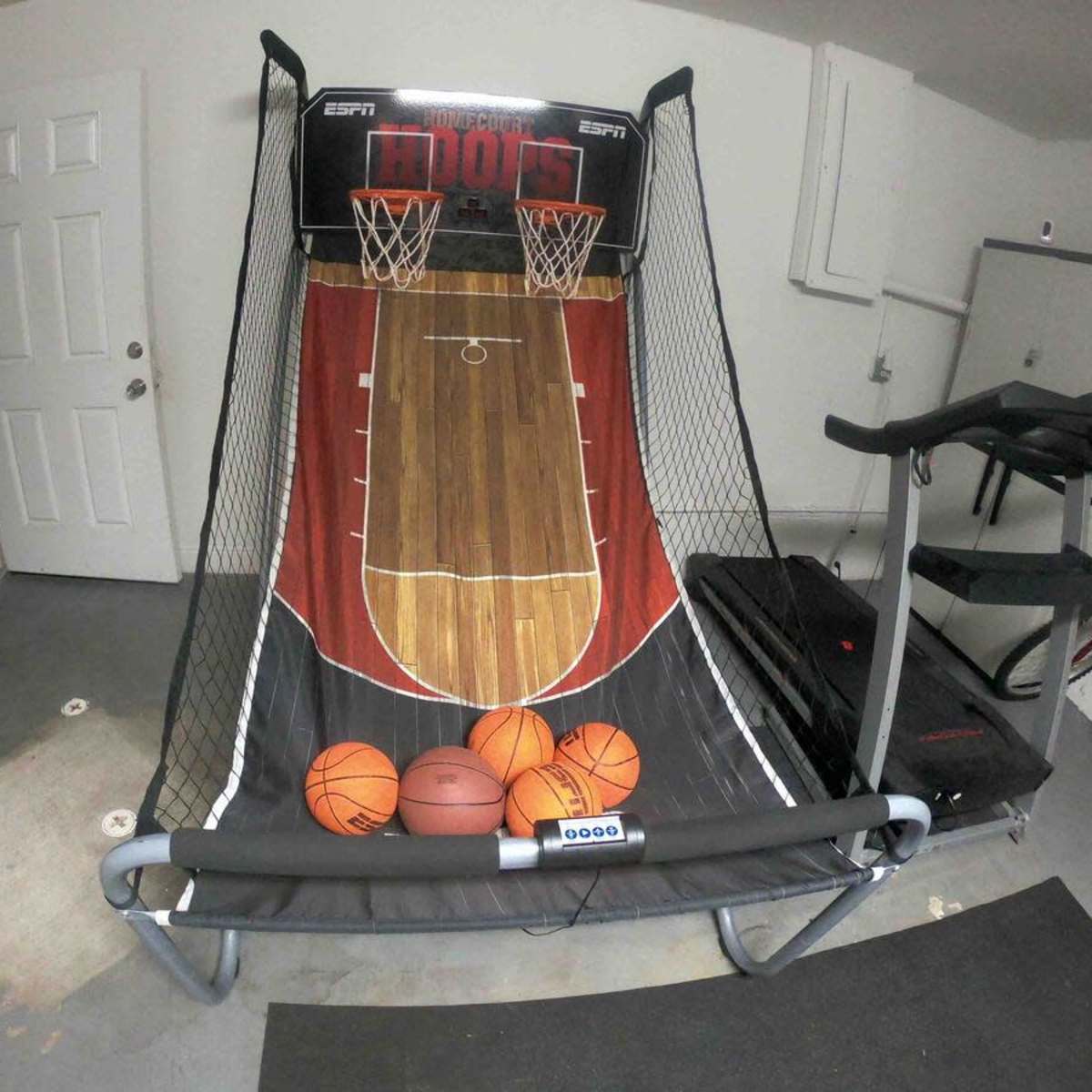 An indoor basketball arcade game set up against a wall, with several basketballs resting in front of it.