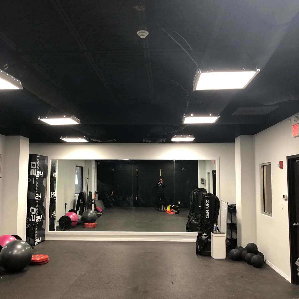 A fitness training room with a large mirror, various exercise equipment, and a black ceiling.