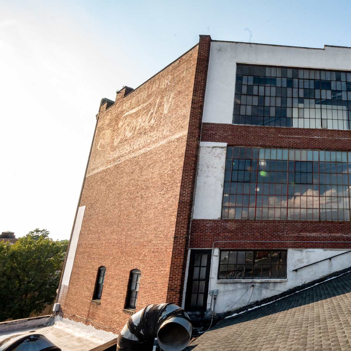 The rear view of a brick building with large windows and an external fire escape, situated adjacent to a sloped roof.