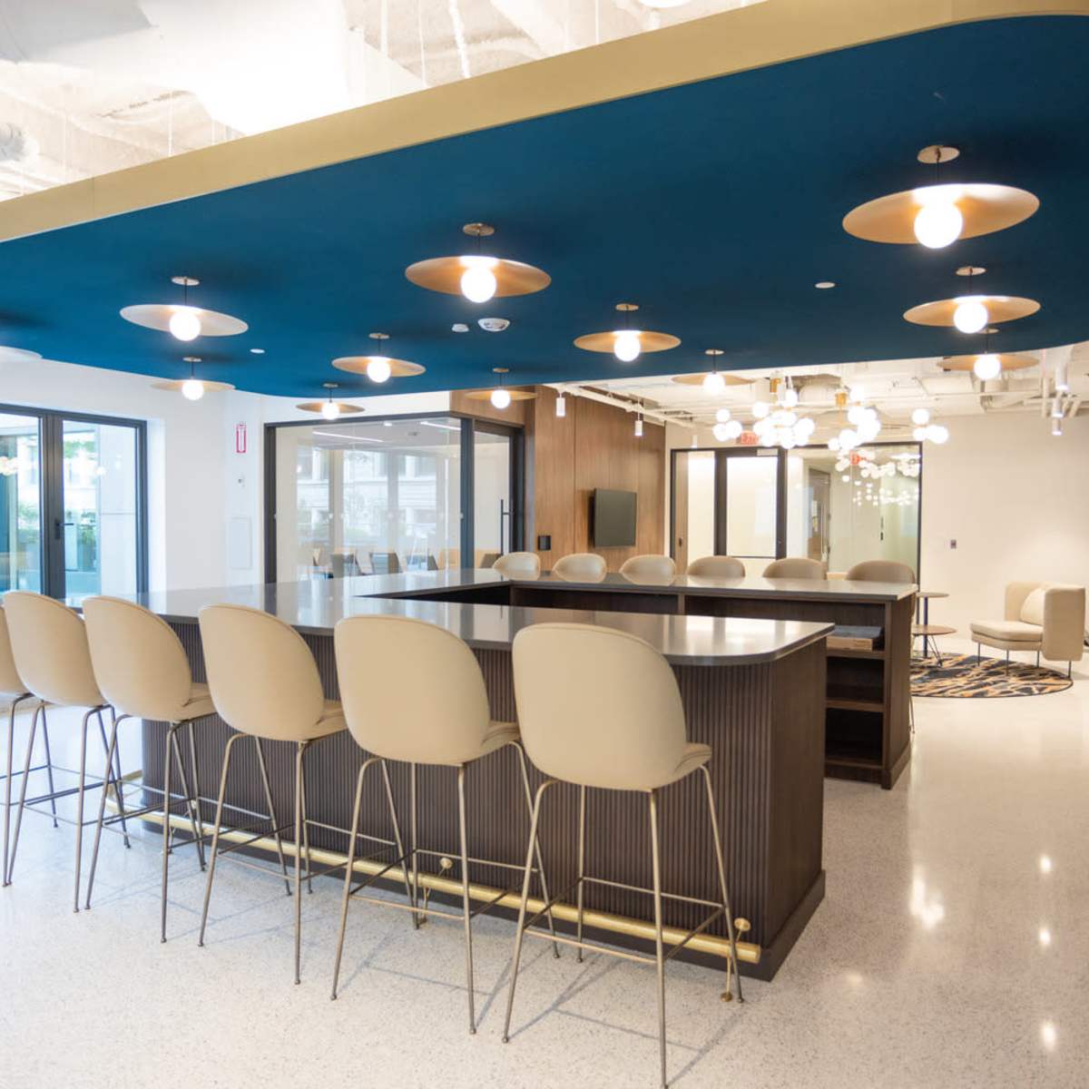 A modern, brightly lit kitchen and dining area with a large island, seating for multiple people, and stylish overhead lighting.