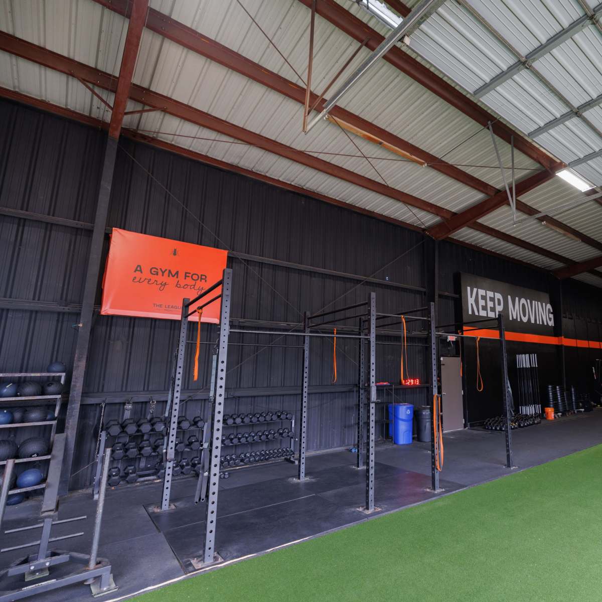 A spacious gym interior with weightlifting equipment, exercise mats, and motivational signage on the walls.