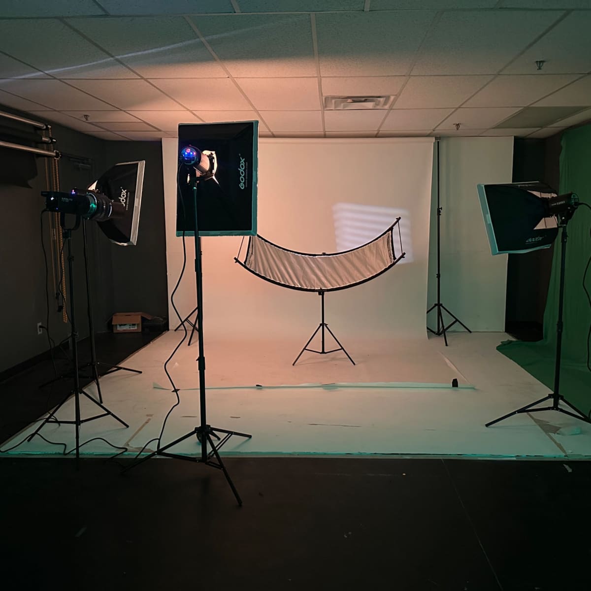 A photography studio setup with two lighting stands, a green backdrop, and a large light diffuser on a tripod in the center against a white background.