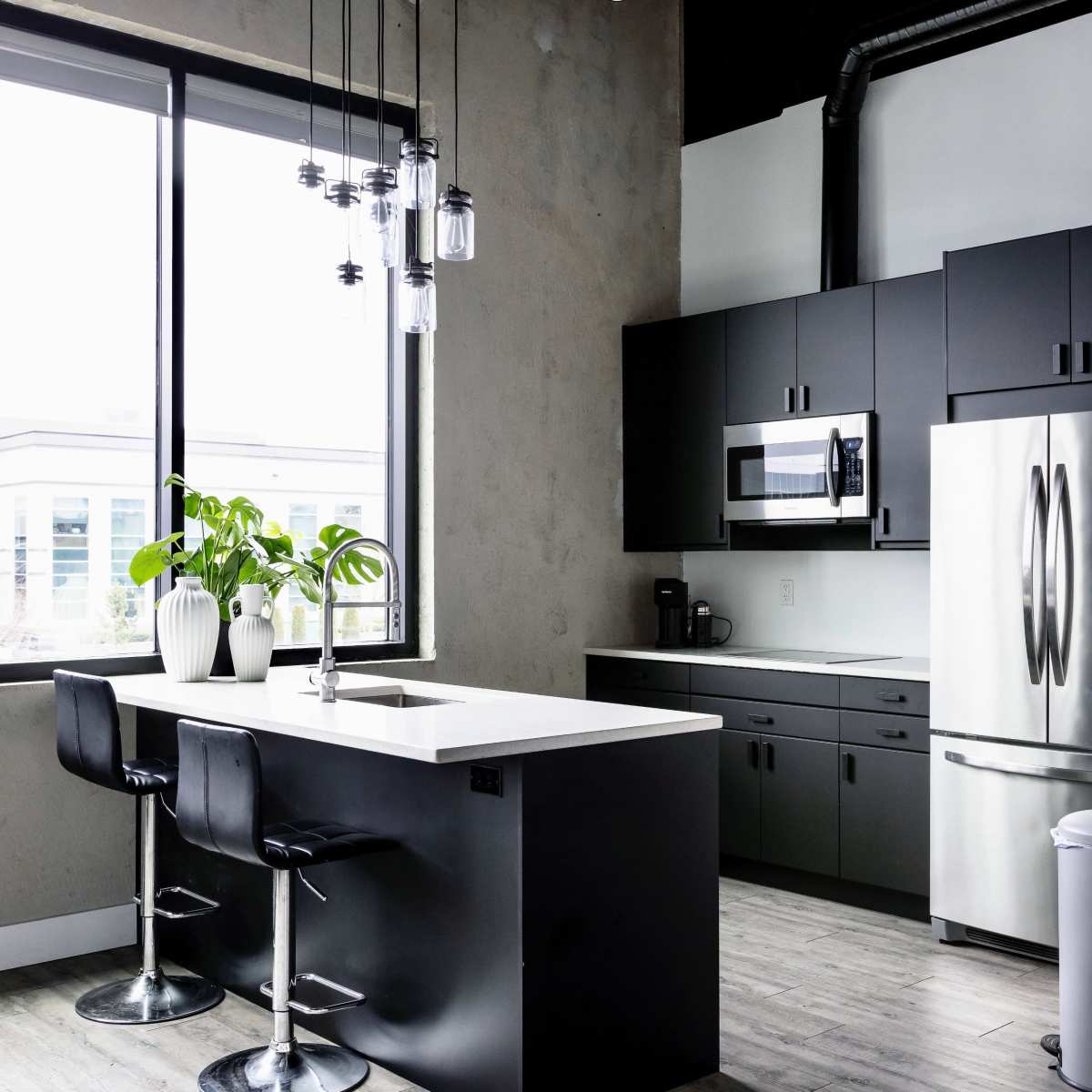 A modern kitchen features black cabinetry, a large window, a white countertop, and a bar with black stools.