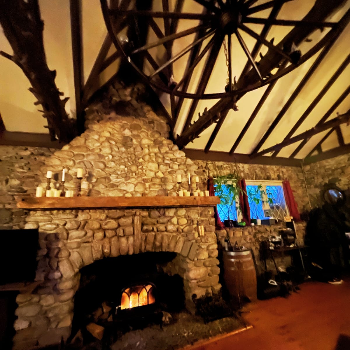 A stone fireplace with a wooden mantel in a rustic room, highlighted by a large chandelier and stained glass windows.
