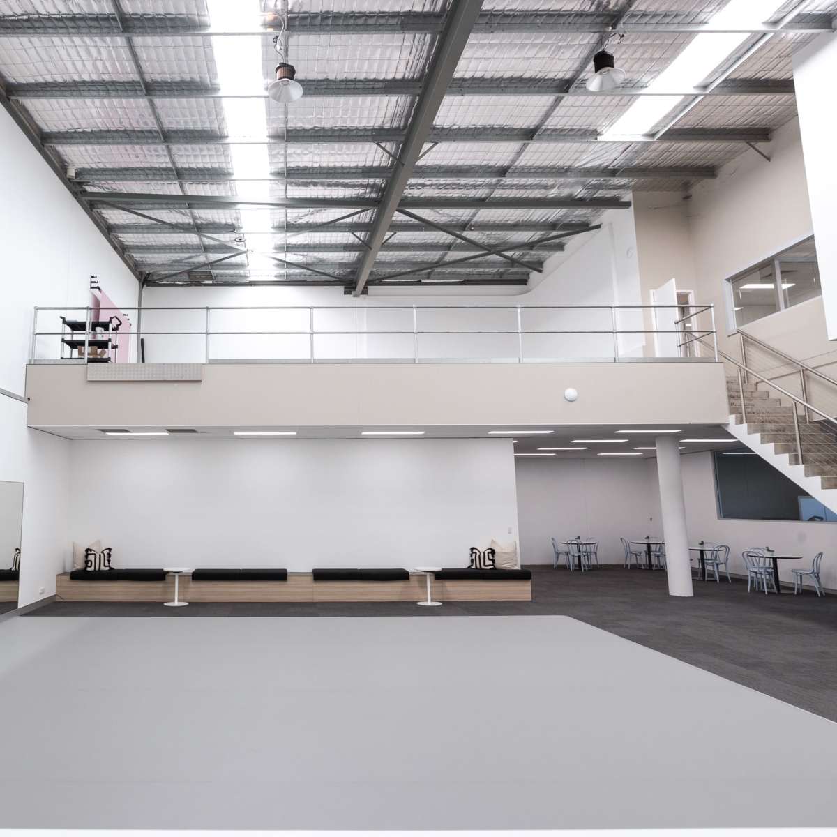 A spacious, brightly lit dance studio with a mirrored wall, a gray floor, and a mezzanine level overlooking the main area.
