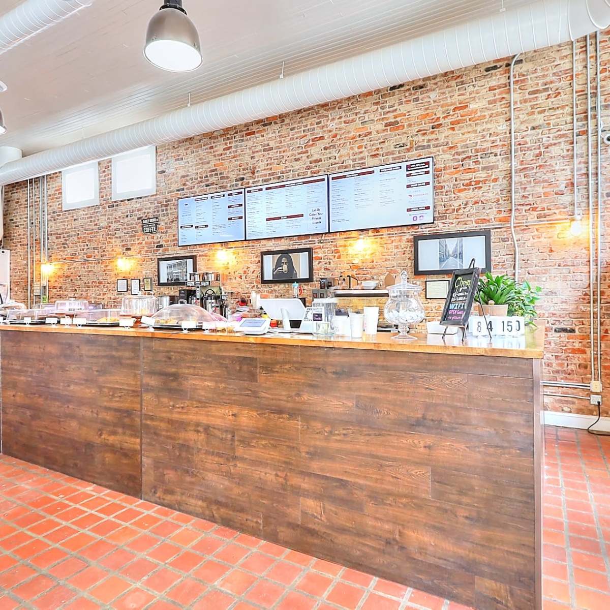 A rustic café interior with a wooden counter, exposed brick walls, and a display of beverages in a glass refrigerator.