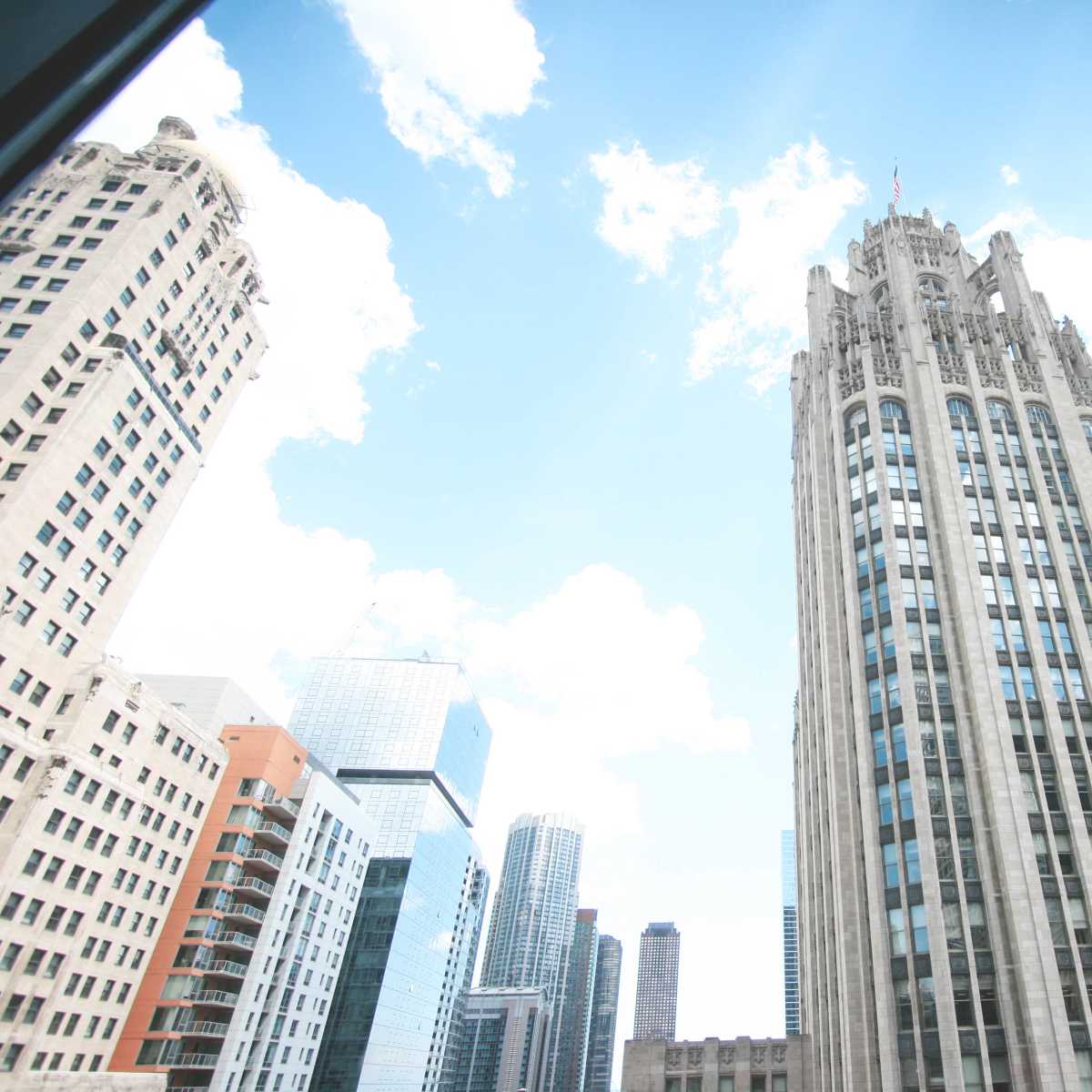 A view of tall skyscrapers with a prominent Art Deco building in the foreground under a clear blue sky.