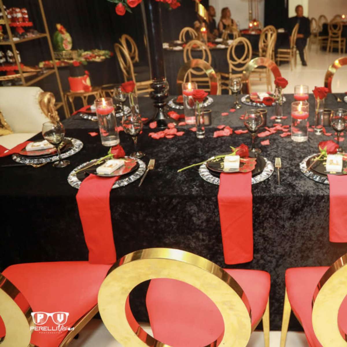 A formal dining table is elegantly set with black and red decorations, including plates, candles, and rose petals.