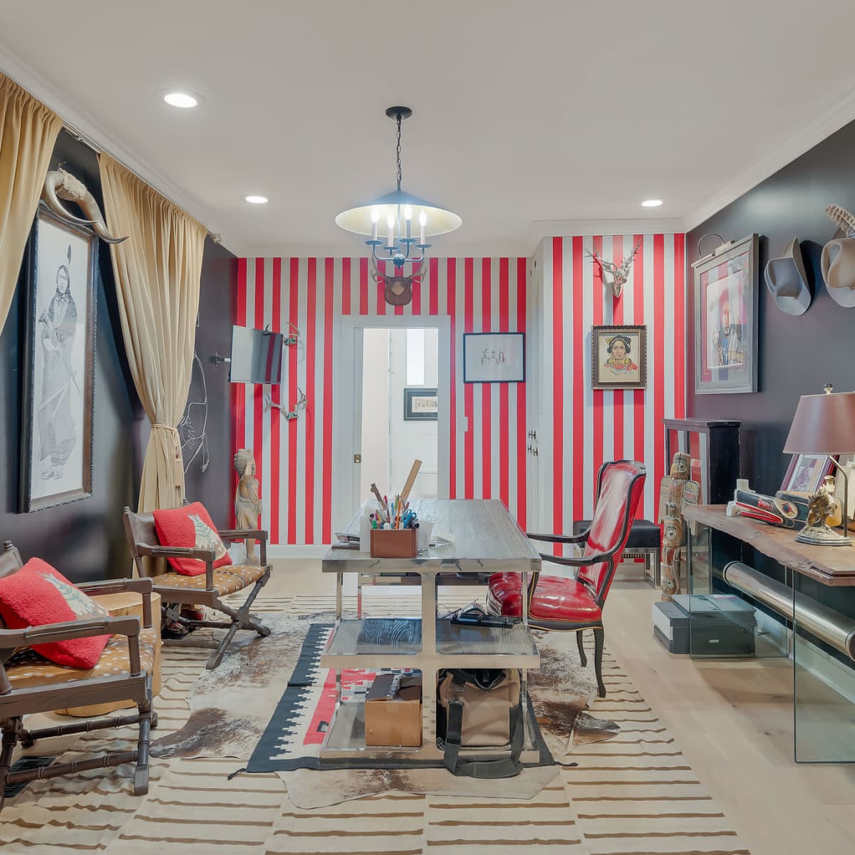 A styled office space with red and white striped walls, wooden furniture, and various decorations, including hats and framed pictures.