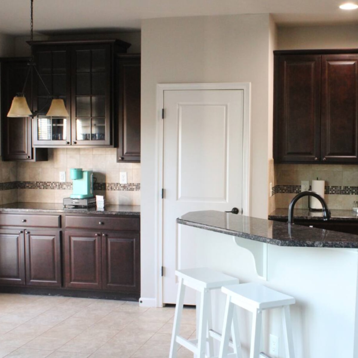 A modern kitchen with dark wood cabinets, stainless steel appliances, and a granite countertop with bar stools.