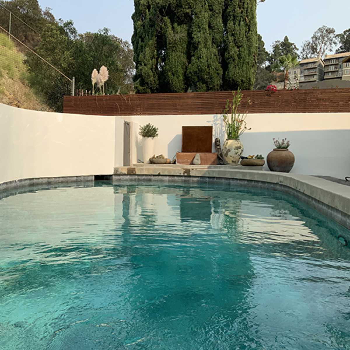 A clear swimming pool surrounded by a white wall, with greenery and decorative elements in the background.