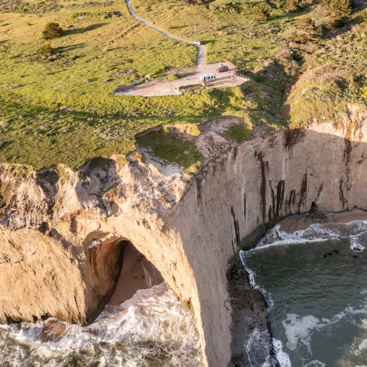 A coastal cliff with a pathway leading to a viewpoint overlooking the ocean waves crashing against the shore.