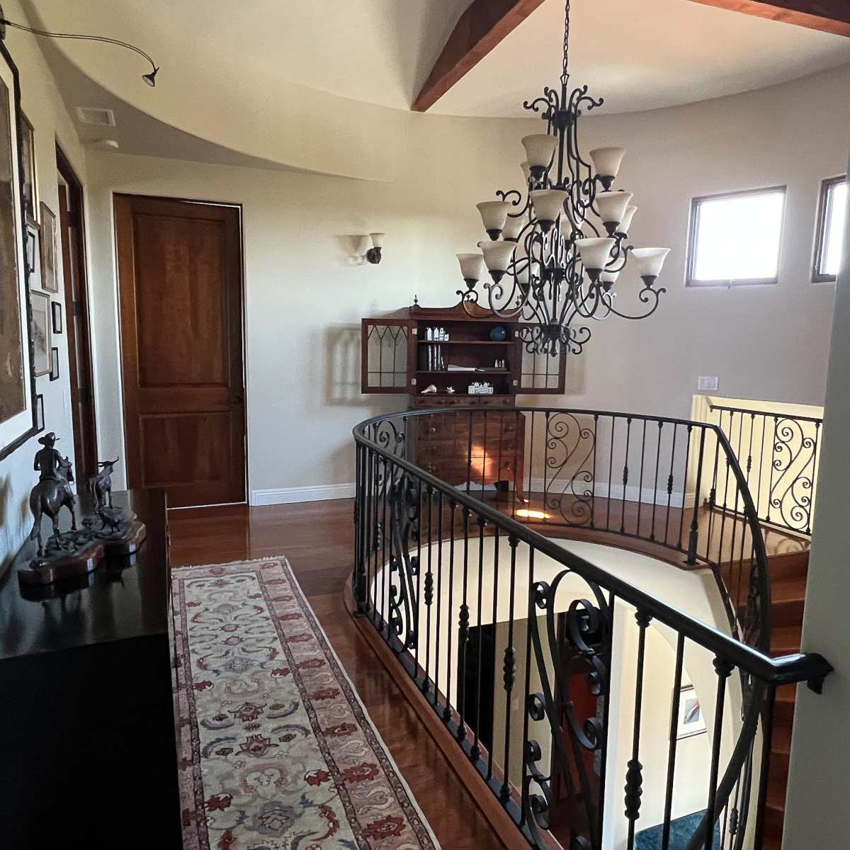 A hallway with a curved staircase, a wooden door, a chandelier, wall art, and a small shelf against the wall.