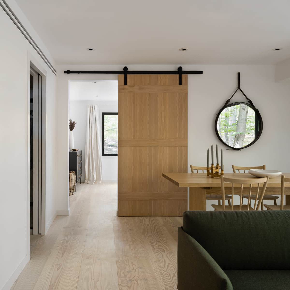 A modern interior featuring a sliding wooden door, an open dining area with a table and chairs, and light-colored walls with a wooden shelving unit.