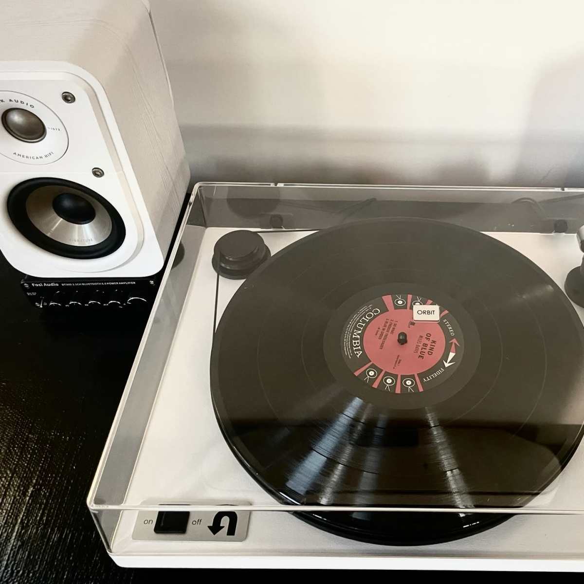 A record player is placed on a table with two speakers on either side, featuring a vinyl record positioned on the turntable.