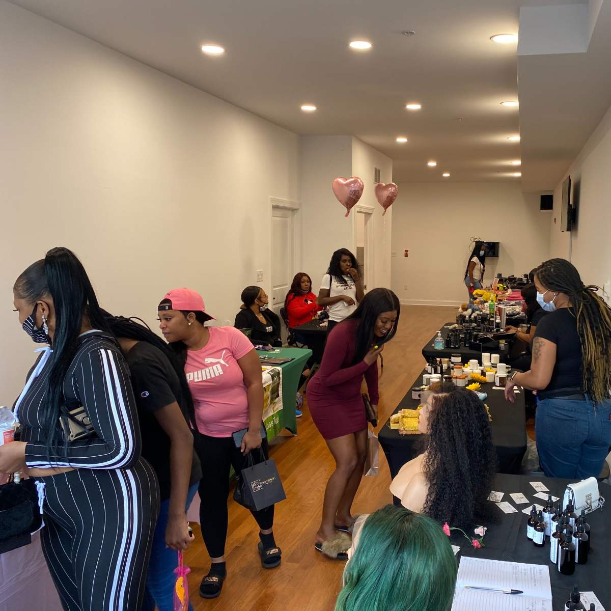 A bustling event space with people browsing tables displaying beauty products and services.