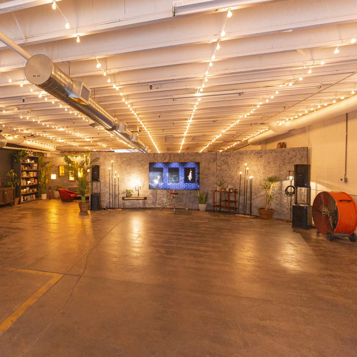 A spacious indoor area with string lights, a basketball hoop, seating, shelves, and a large screen on the wall.