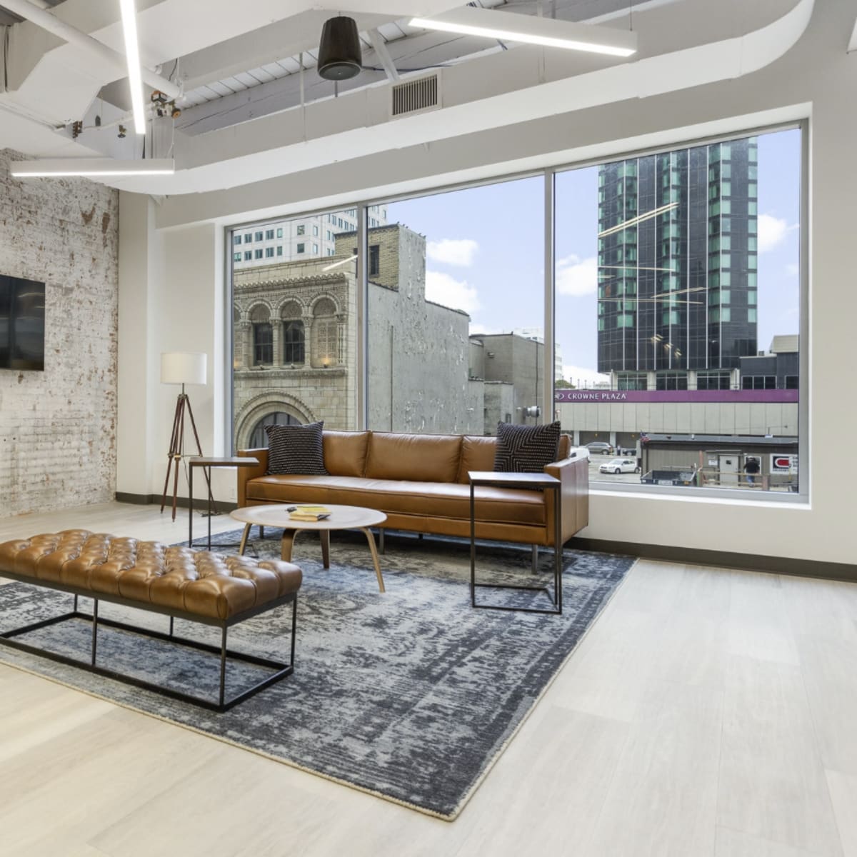 A modern interior living space with a leather sofa, an ottoman, a coffee table, and a large window overlooking a cityscape.