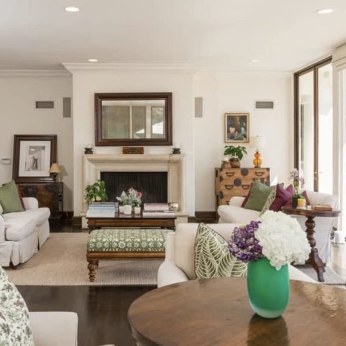 A light-filled living room with seating arrangements, a fireplace, and large windows overlooking a pool area.