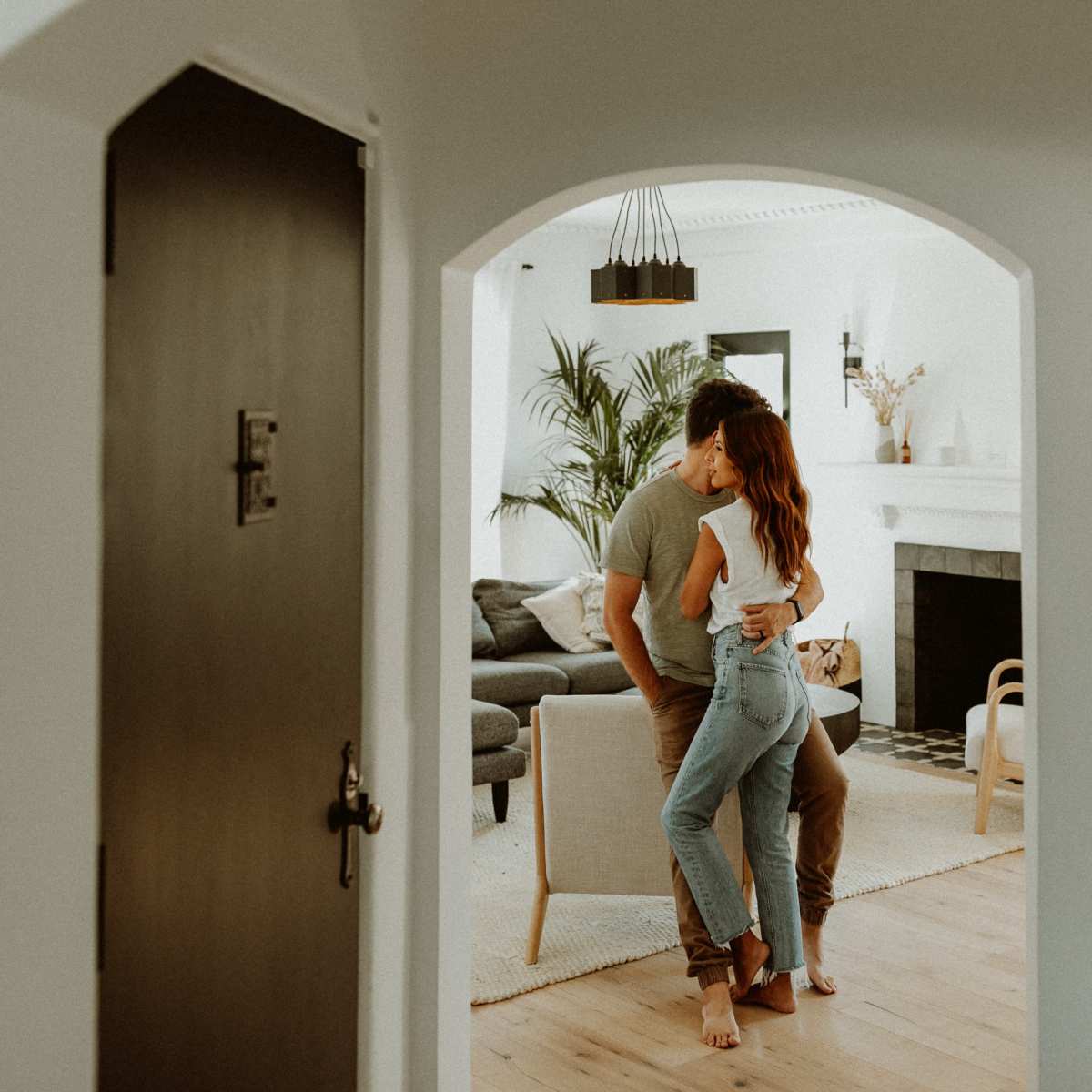 A couple shares a close embrace in a spacious living room framed by an arched doorway.