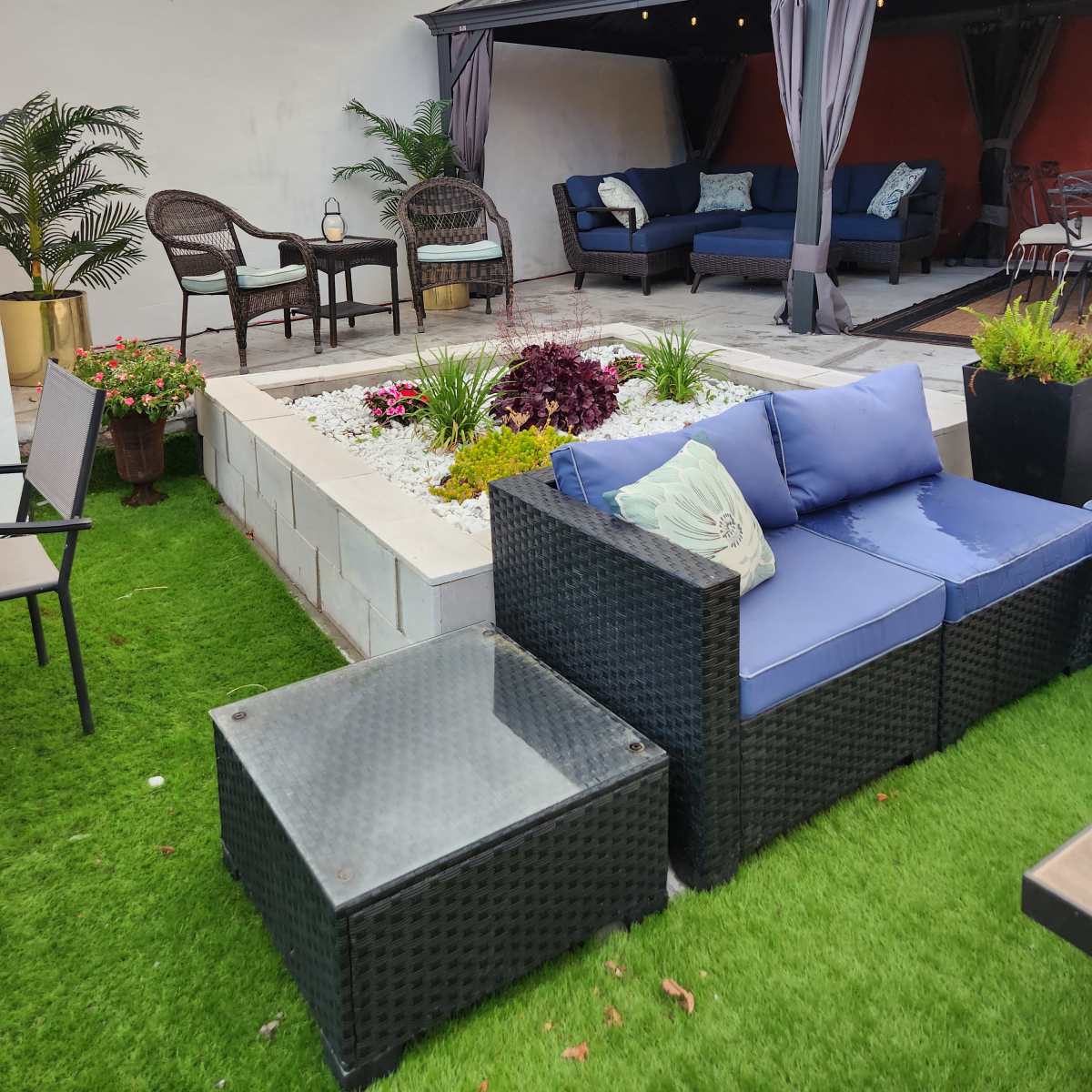 A landscaped outdoor patio area featuring a seating arrangement with blue cushions, a small coffee table, and surrounding greenery.