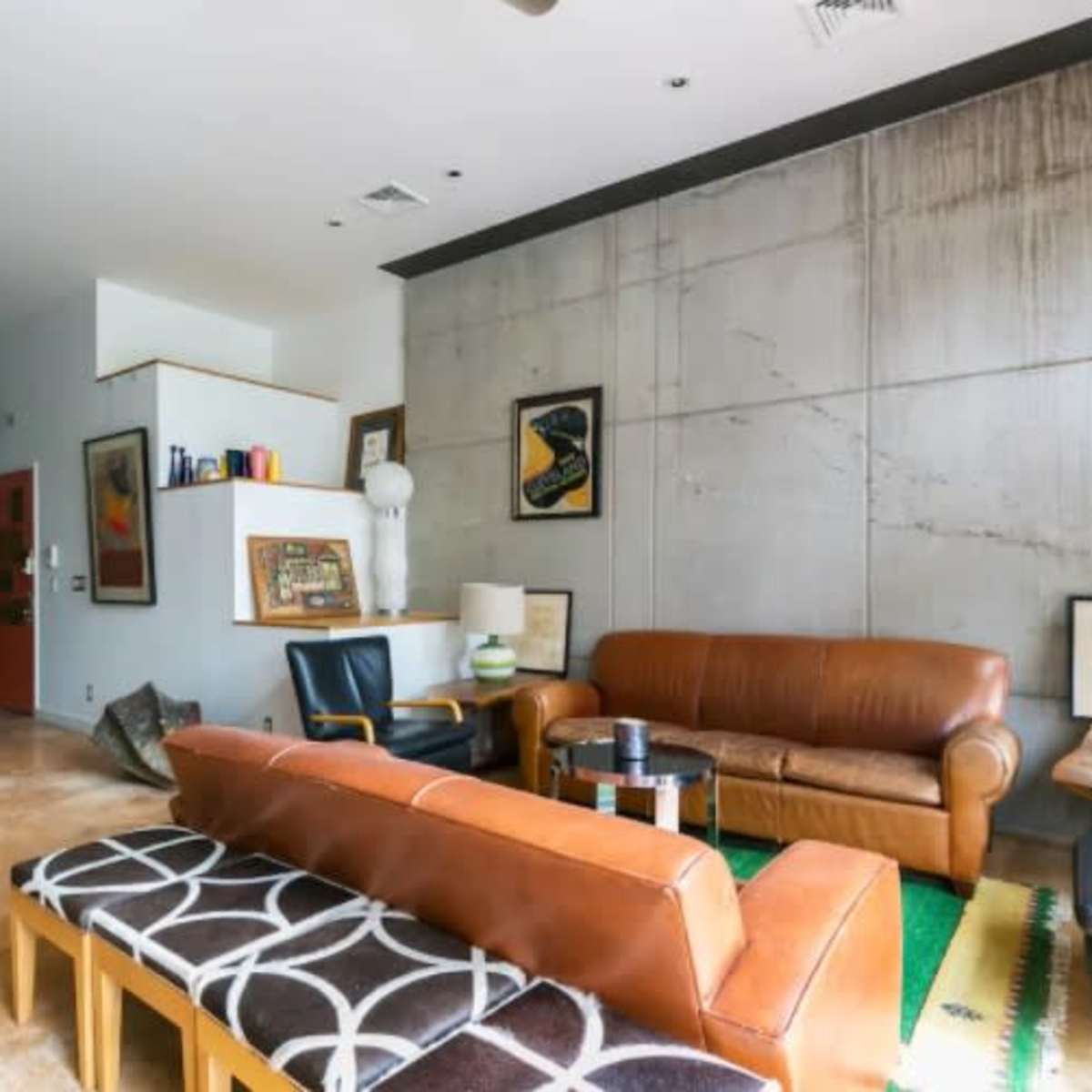 A spacious living area featuring a brown leather sofa, mid-century chairs, a concrete wall, and a dining table with wooden chairs.