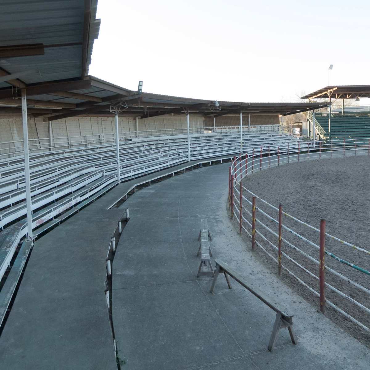 A partially empty rodeo arena with metal bleachers surrounding a circular dirt floor.