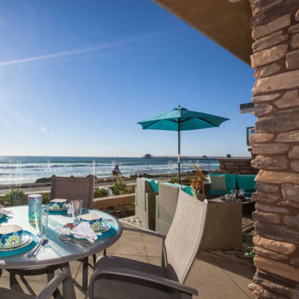 A patio dining set is positioned near the beach, overlooking the ocean with sun shining brightly in the background.