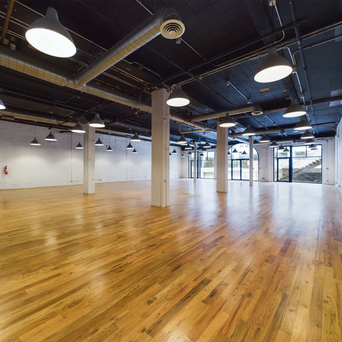 A large, empty industrial-style room with hardwood floors and overhead lighting.