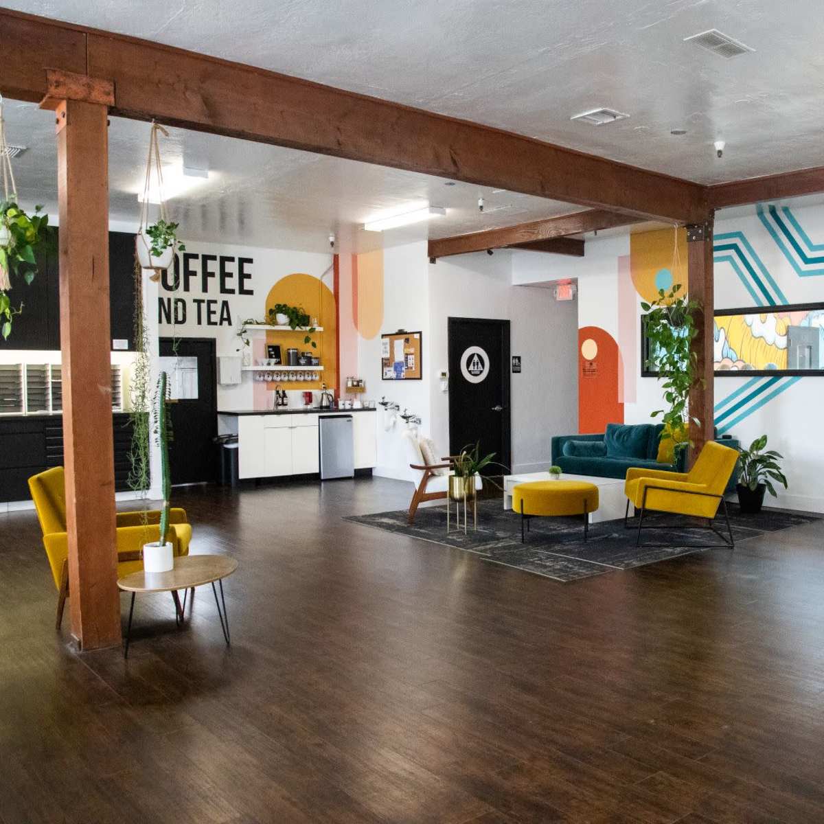 A spacious, modern interior with wooden beams, colorful wall designs, a seating area featuring yellow chairs, and a coffee and tea station.