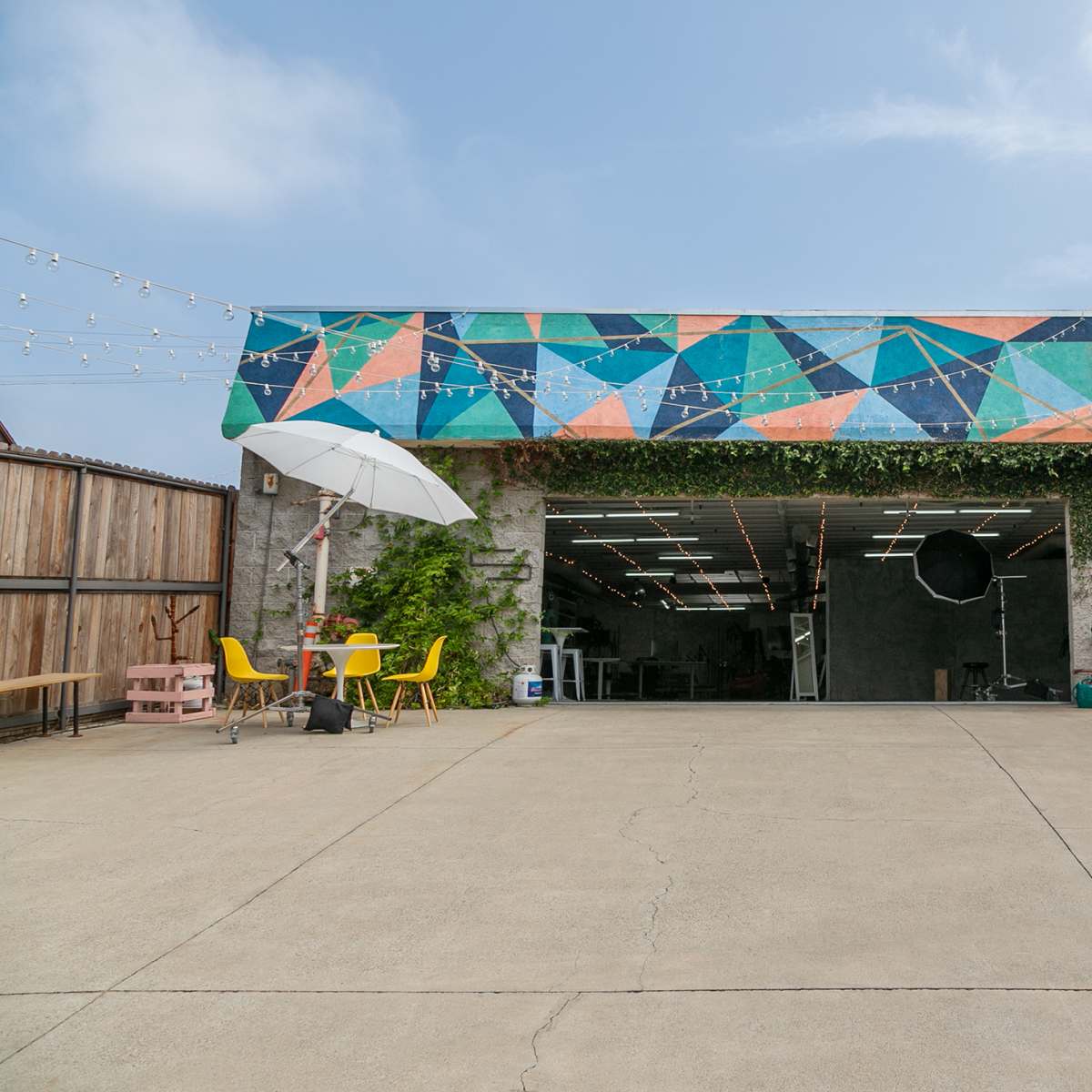 A spacious garage with a colorful geometric mural on the roof, surrounded by greenery and featuring patio furniture in front.