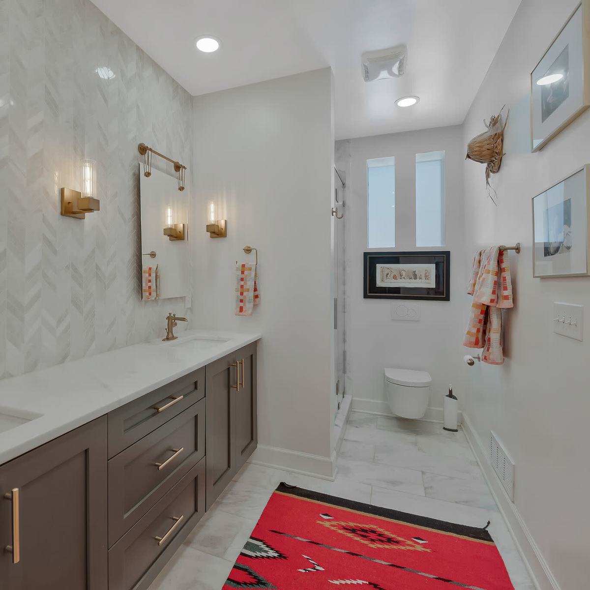 A modern bathroom featuring a double vanity with gold fixtures, a large mirror, a striped rug, and a glass-enclosed shower area.