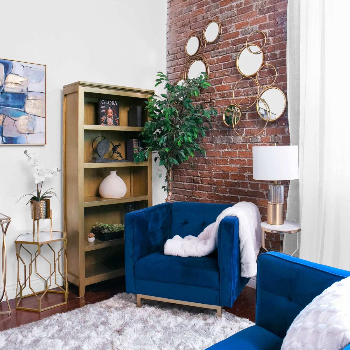 A cozy living room features blue upholstered chairs, a gold bookshelf with decorative items, and a window letting in natural light.