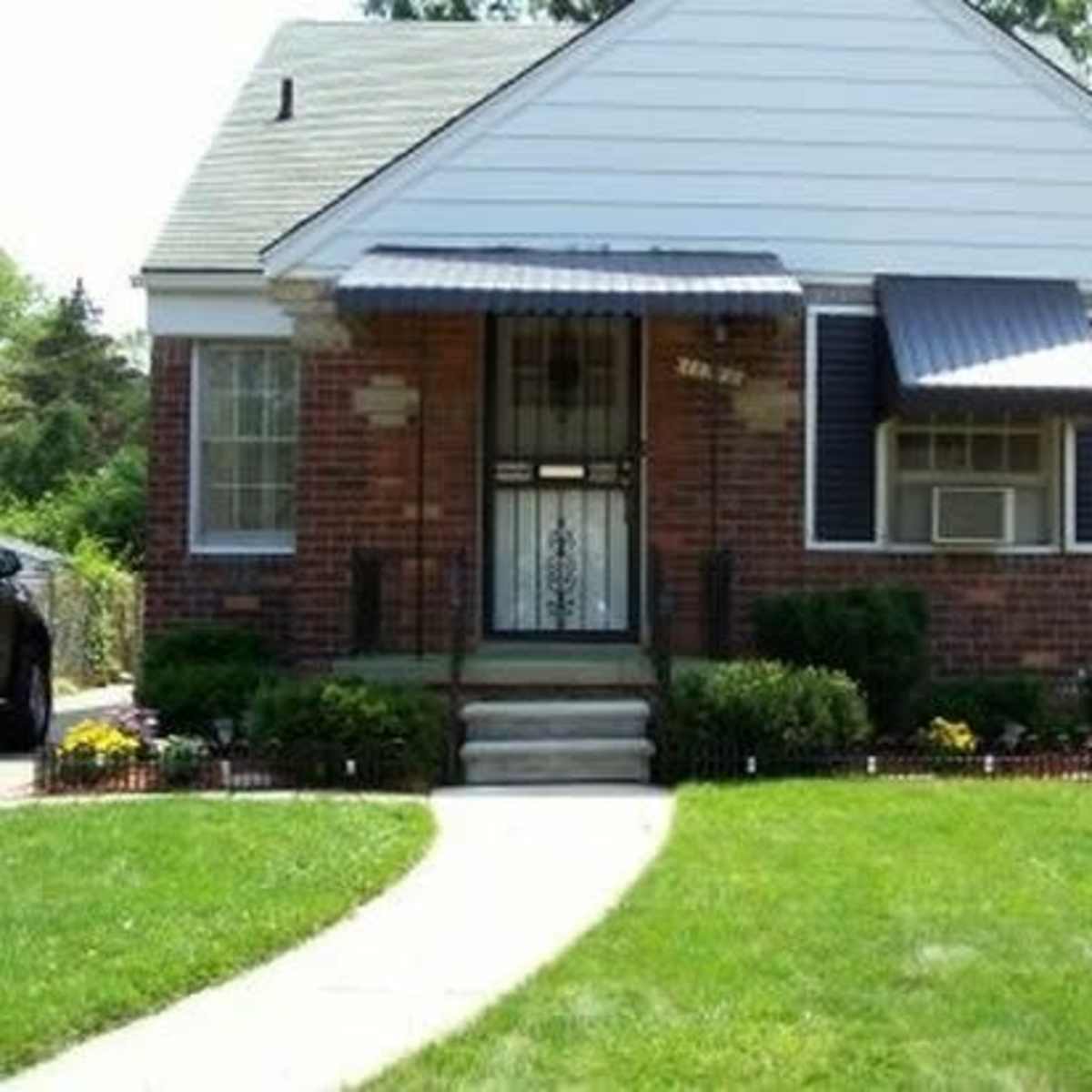 A brick house with a white upper facade and a front porch is surrounded by a neatly maintained lawn and flower beds.