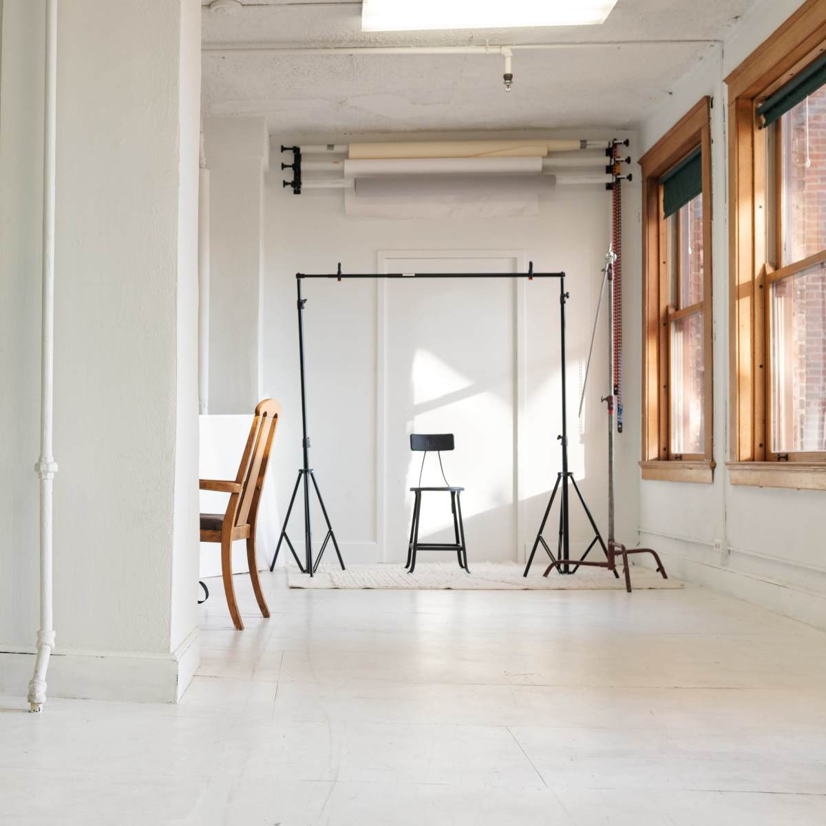 A spacious room features a chair on a backdrop stand, flanked by large windows and a potted plant in the corner.