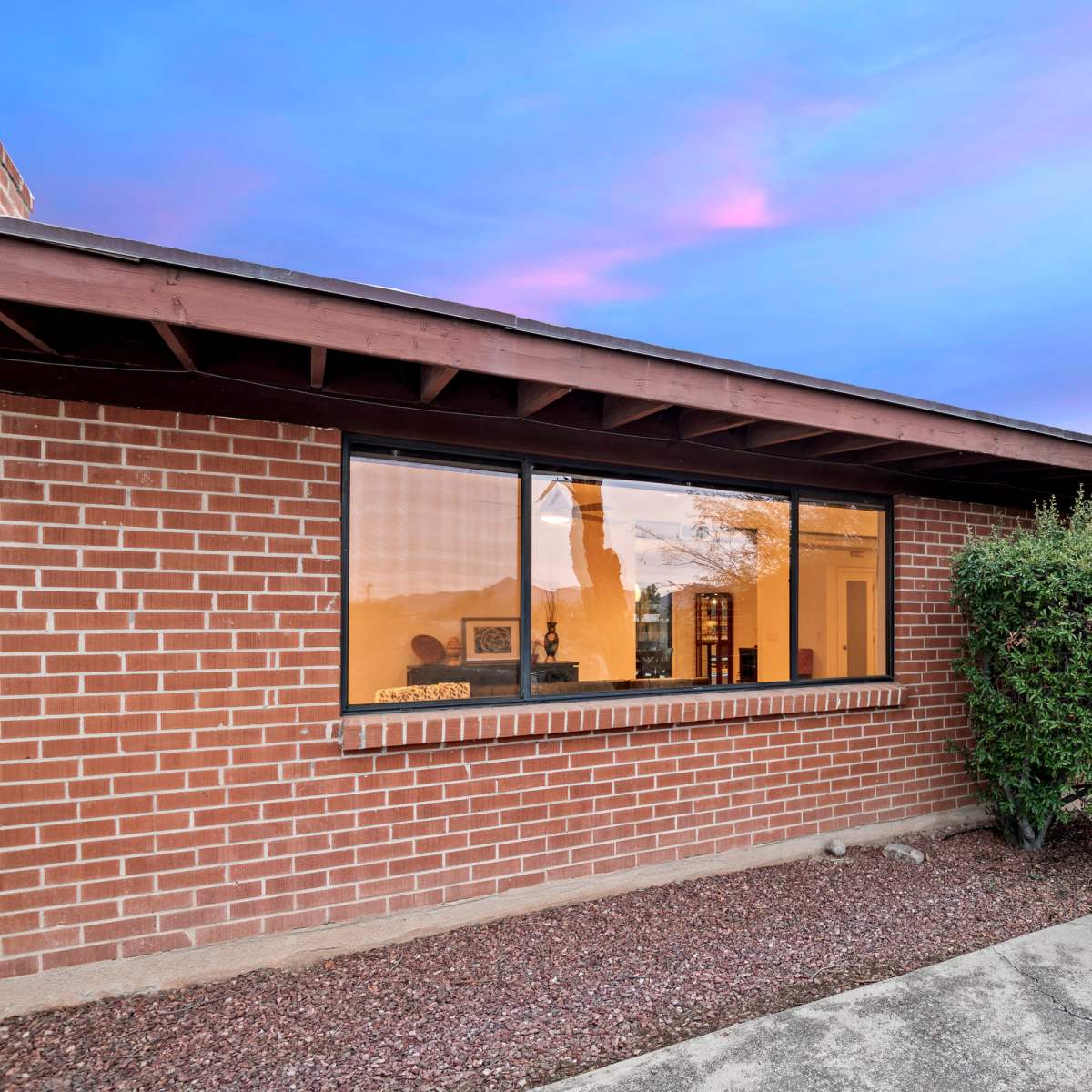 A single-story brick building with large windows is surrounded by neatly trimmed bushes and a walkway.
