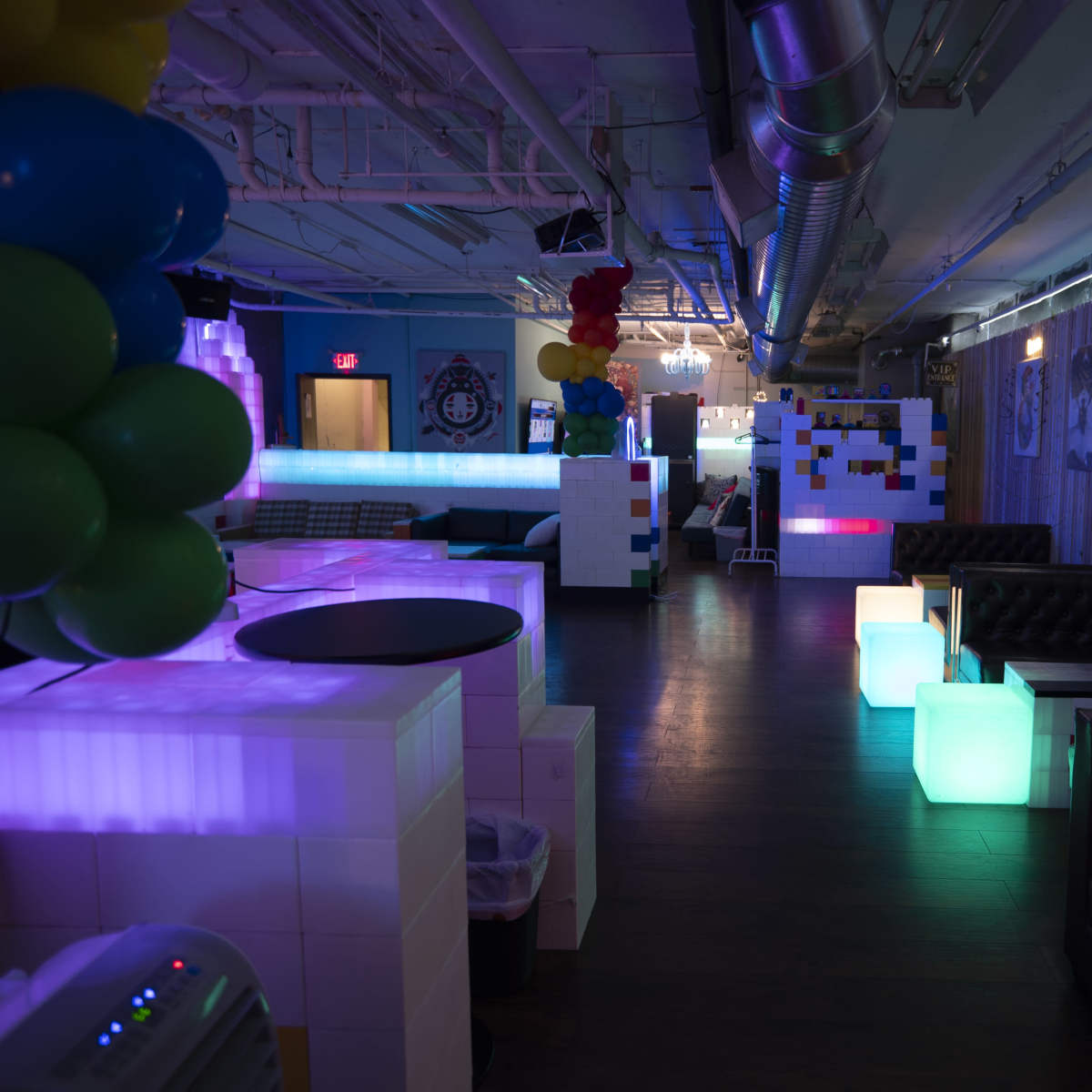 A brightly lit lounge area with illuminated furniture and decorative elements, featuring a mix of sofas and sectioned spaces.
