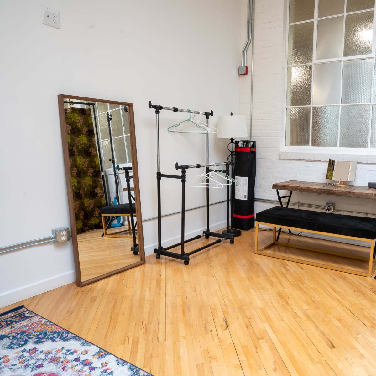 A minimalist room featuring a full-length mirror, a clothing rack, a wooden bench, and a window with frosted glass.