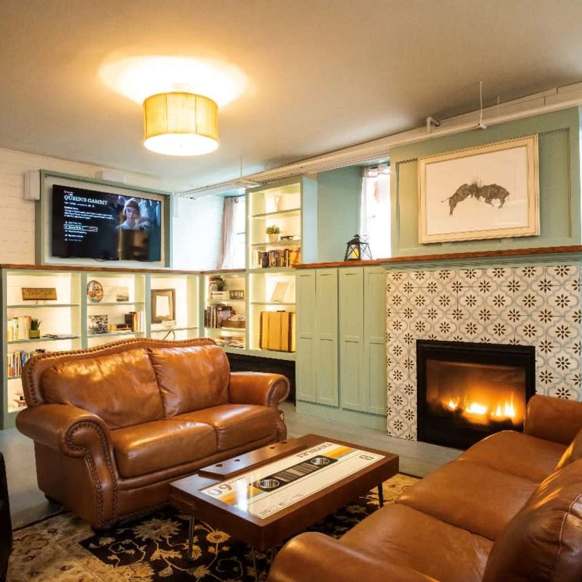 A cozy living room featuring two brown leather sofas, a decorative fireplace with tiled accents, a television mounted on the wall, and built-in shelves filled with books and decorative items.