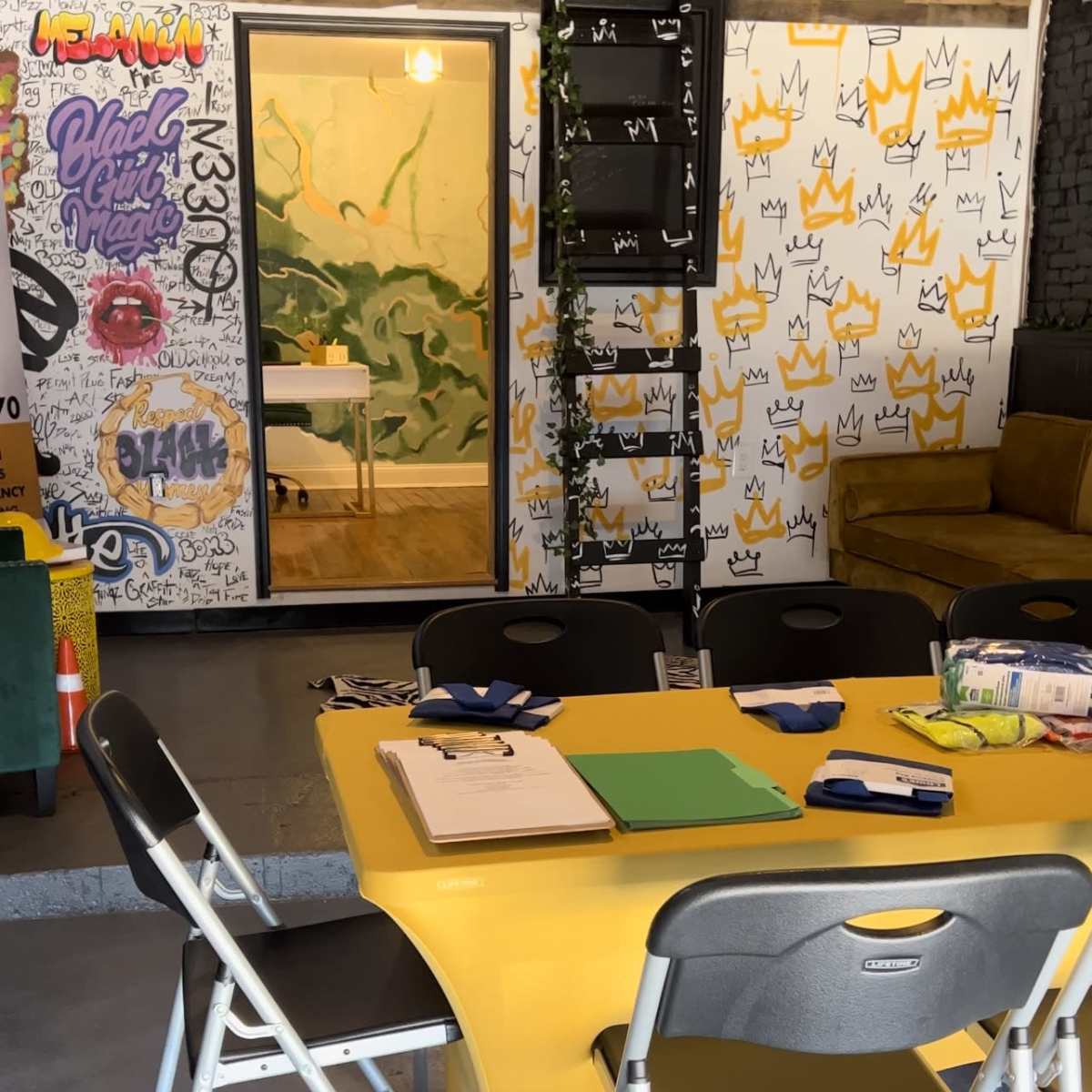 A yellow table surrounded by metal chairs sits in a creatively decorated room with a visible doorway leading to another area.