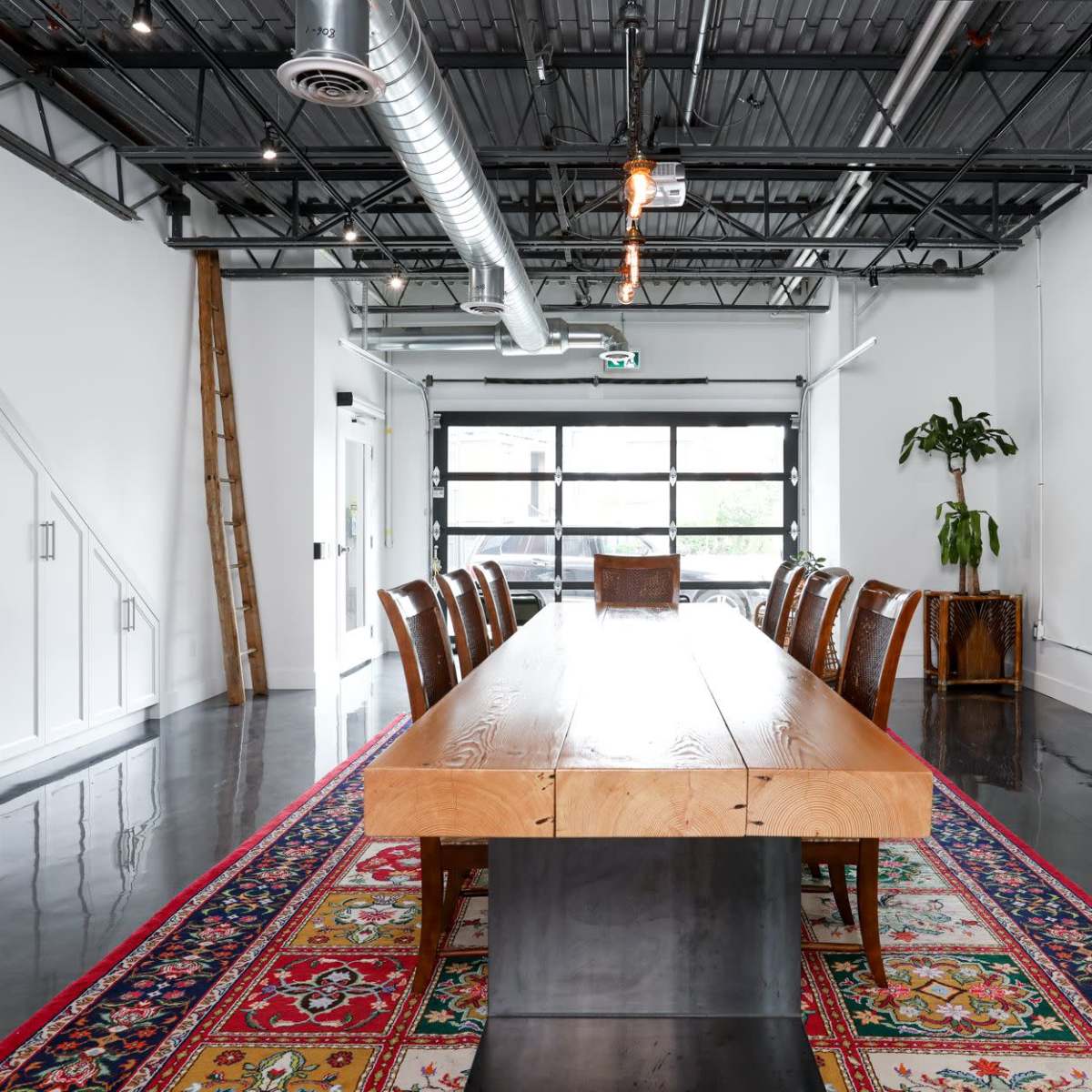A modern conference room with a long wooden table, surrounded by brown chairs, located in a space with high ceilings and large windows.