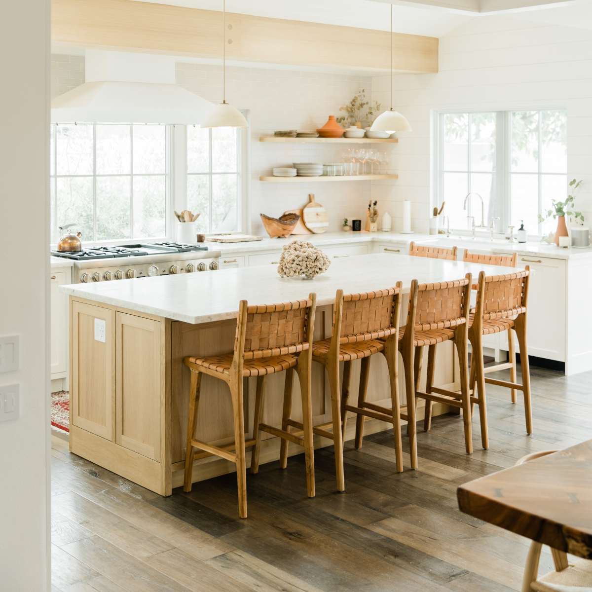 A modern kitchen with a large island, wooden bar stools, and a white countertop under natural light from windows.